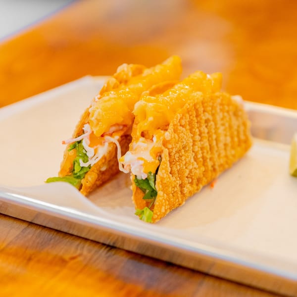 Two crispy fried tacos filled with lettuce, white sauce, and melted cheese on a white tray.