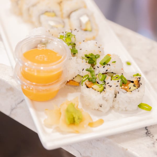 Nooki sushi rolls with green onions, sesame seeds, ginger, wasabi, and orange sauce.