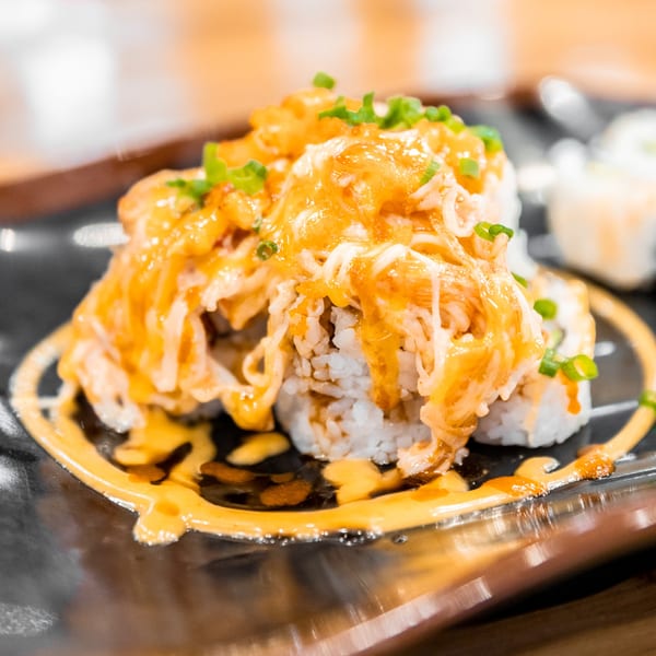 Nooki sushi rolls topped with orange sauce, shredded crab, and green onions on a black plate.