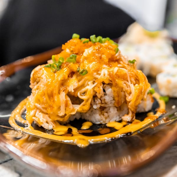 Nooki's sushi roll topped with orange sauce, crab meat, fish roe, and green onions.
