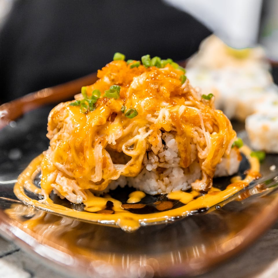 Nooki's sushi roll topped with orange sauce, crab meat, fish roe, and green onions.